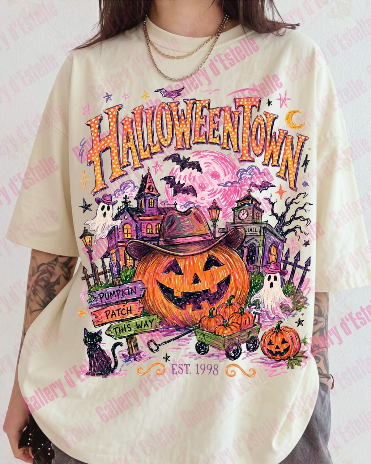A person wearing an oversized cream-colored graphic t-shirt with a colorful Halloween-themed print featuring pumpkins, haunted houses, bats, and the text 'Halloween Town'.