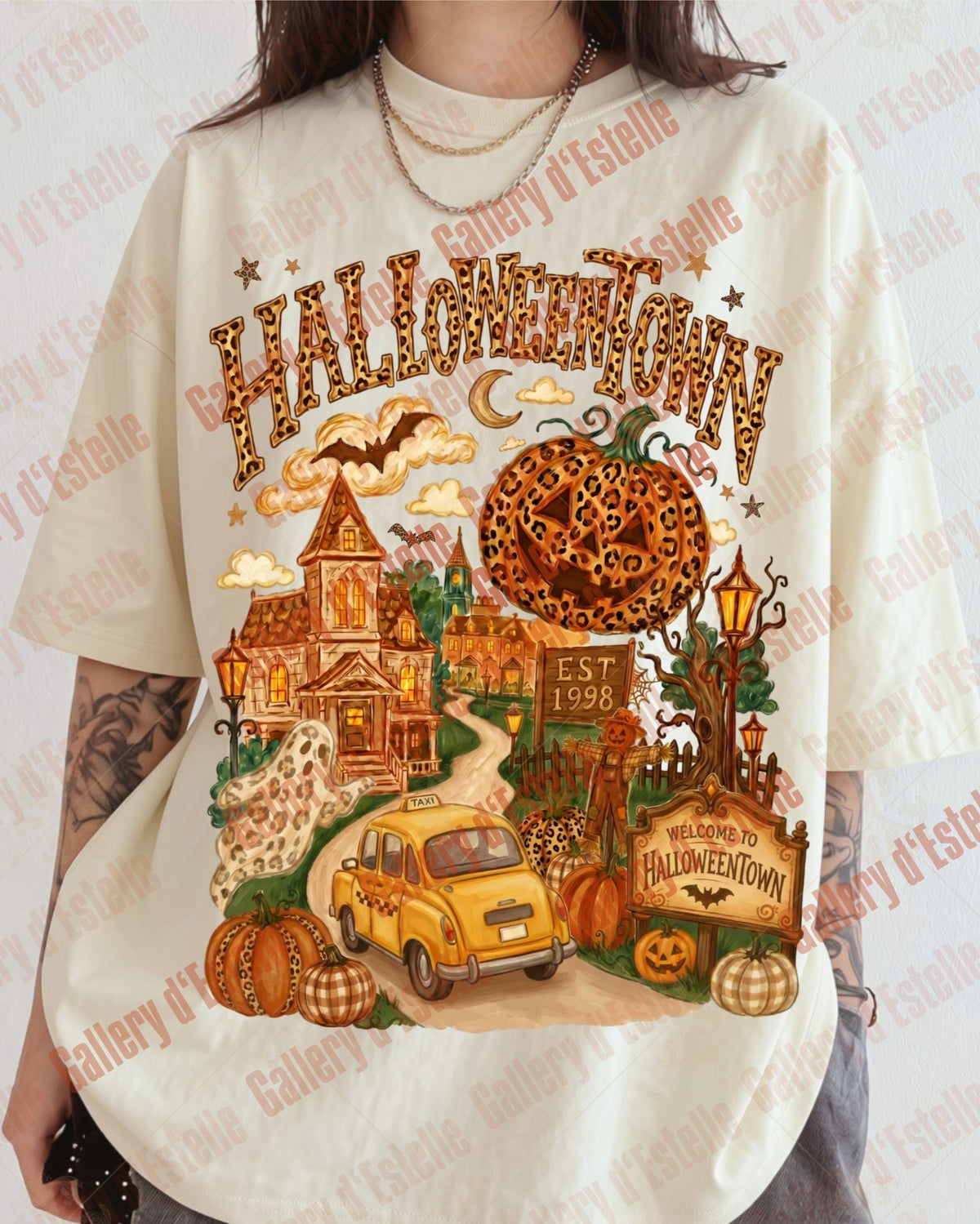 A person wearing an oversized cream-colored graphic t-shirt featuring a colorful Halloween-themed illustration with the word 'HALLOWEOWN' in leopard-print lettering, a haunted house, a yellow car, pumpkins, and a spooky tree.