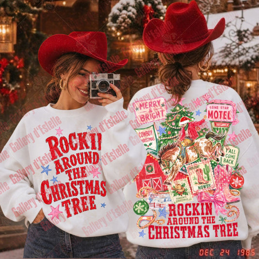 Two women wearing matching white sweatshirts with a red and multicolor 'Rockin' Around the Christmas Tree' graphic, styled with red cowboy hats in a festive outdoor holiday setting.