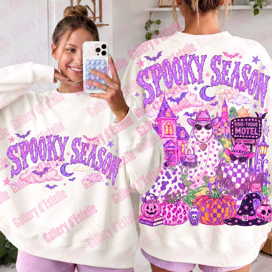 A white crewneck sweatshirt with a colorful 'Spooky Season' Halloween graphic, shown from both the front and back on a model. The design features purple text, cowgirl ghosts, pumpkins, a haunted house, and bats.