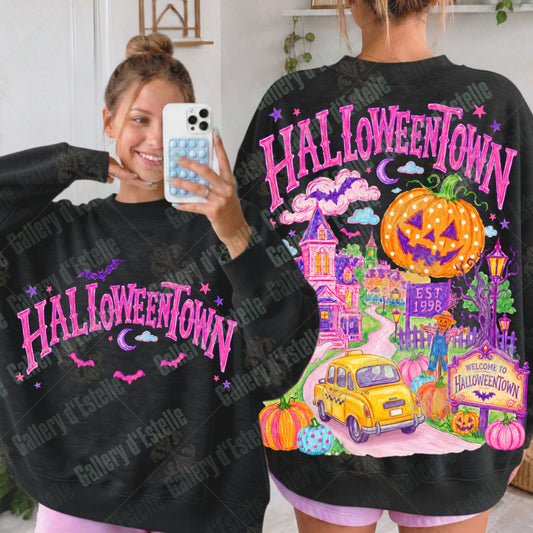 A woman shown from the back wearing a black sweatshirt with a large colorful Halloween-themed graphic that reads HALLOWEENTOWN, alongside a mirror selfie showing the front of the same sweatshirt. The design includes pink lettering, a jack-o'-lantern, purple clouds, a yellow car, and pumpkins on a light indoor background.
