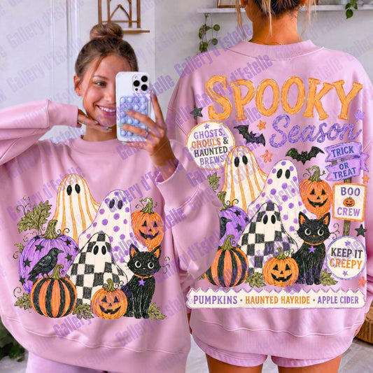 A pink crewneck sweatshirt shown from both front and back on a model. The front features a Halloween graphic with pumpkins, ghosts, a black cat, and a crow.
