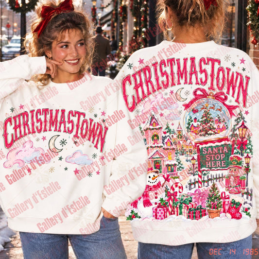 A vintage Christmas-themed sweatshirt shown from both front and back on a model. The white crewneck sweatshirt features 'CHRISTAMASTOWN' in red arched letters on the front, with a colorful winter village scene on the back.