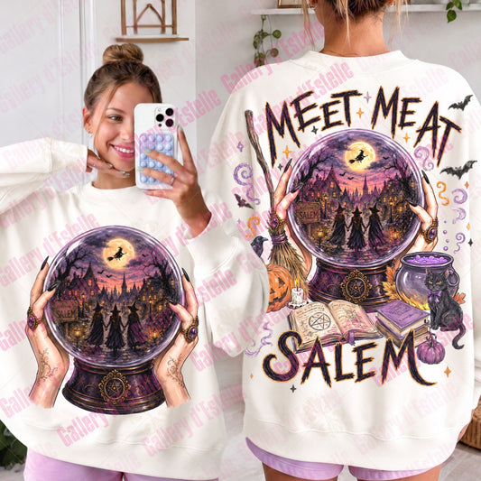 A white crewneck sweatshirt with a large Halloween-themed graphic print, shown from both the front and back on a model. The front features a crystal ball design with a witch and crows, while the back displays the text 'MEET MEAT SALEM' with a witch's cauldron and broomstick illustration.