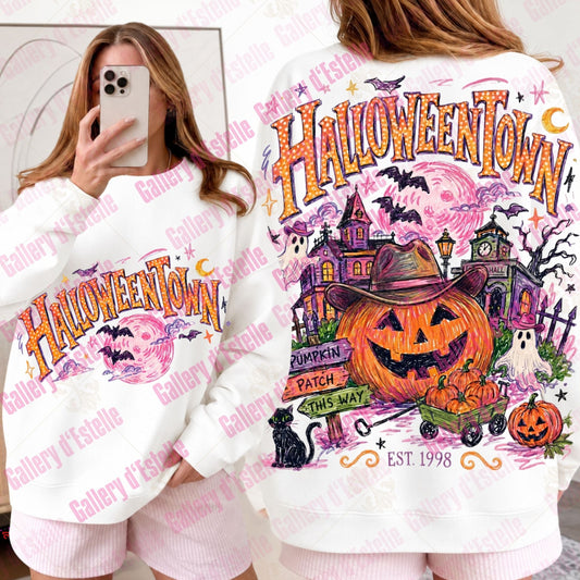 A white long-sleeve sweatshirt with a colorful Western Halloween-themed graphic print featuring 'HALLOWEENTOWN' in orange, a jack-o'-lantern, haunted house, pumpkins, bats, and ghosts. Shown from both front and back on a model, with a pink and white striped skirt.