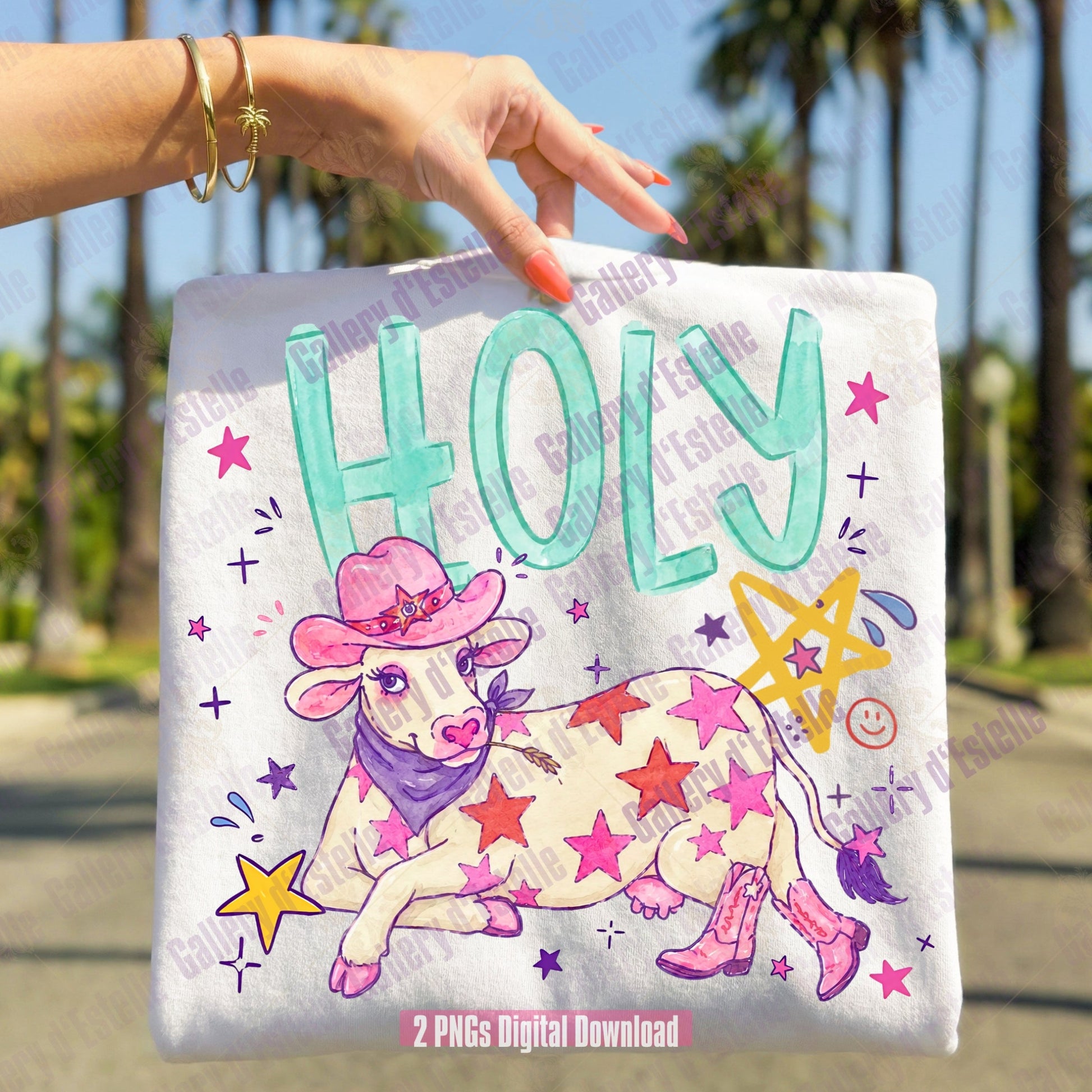 Funny t-shirt  held by a hand with a cowgirl-themed design featuring a cow in a pink hat and boots, surrounded by stars and the word 'HOLY'.