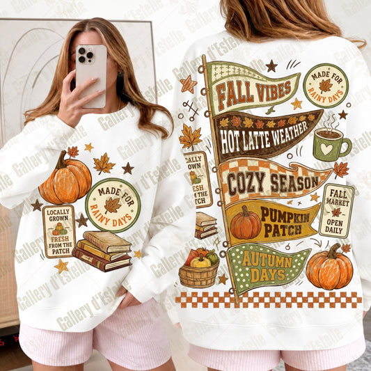 A white long-sleeve sweatshirt with a colorful autumn-themed graphic print, shown in both front and back views. The design features pumpkins, fall leaves, books, a coffee mug, and text like 'Fall Vibes', 'Cozy Season', and 'Autumn Days'.