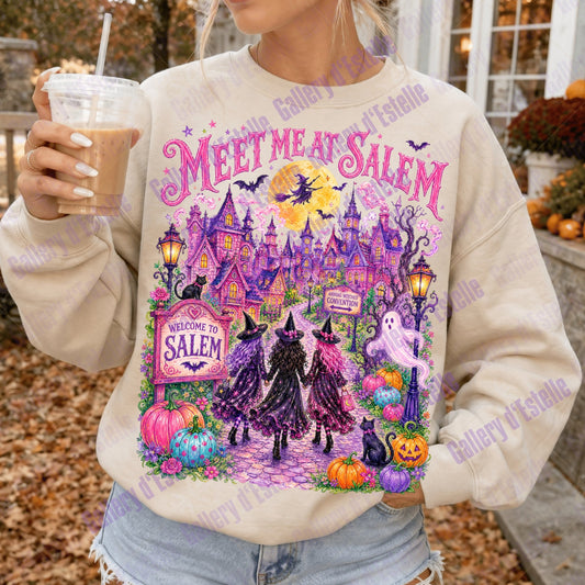 A woman wearing a cream-colored crewneck sweatshirt with a colorful Halloween-themed graphic that reads 'MEET ME AT SALEM' and shows witches, haunted houses, pumpkins, and a full moon. She is holding an iced coffee outdoors.