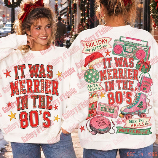 Two women modeling a white sweatshirt with a colorful Christmas 1980s graphic. The front shows the text 'IT WAS MERRIER IN THE 80's' in red with white outline and red stars.