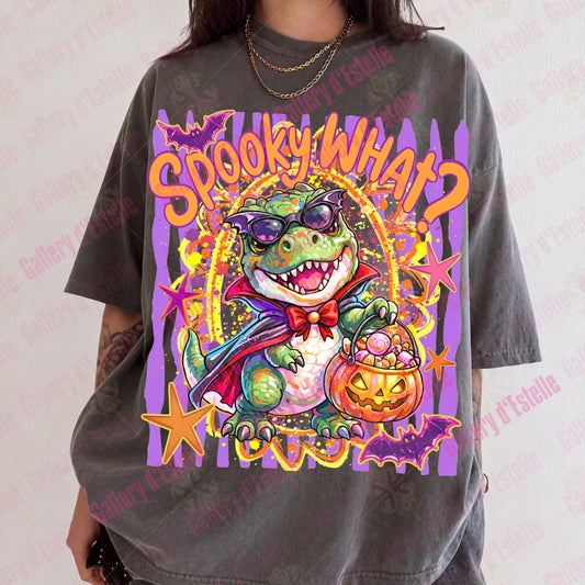 A person wearing an oversized dark gray graphic T-shirt with a colorful cartoon alligator dressed as a vampire holding a jack-o'-lantern, with the text 'Spooky What?' on a purple striped background.