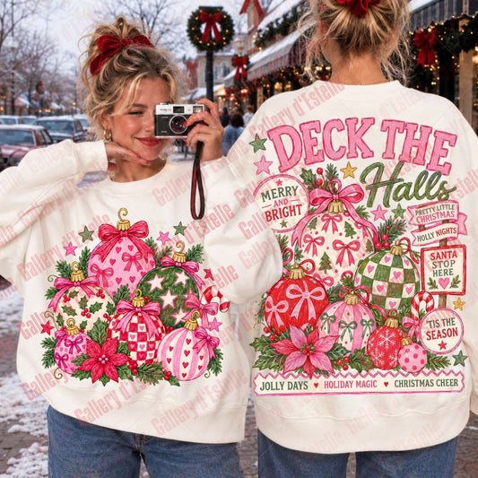Two women modeling a white crewneck sweater with a large pink and green Christmas graphic. The front shows a cluster of pink ornaments, pine branches, and red poinsettias.