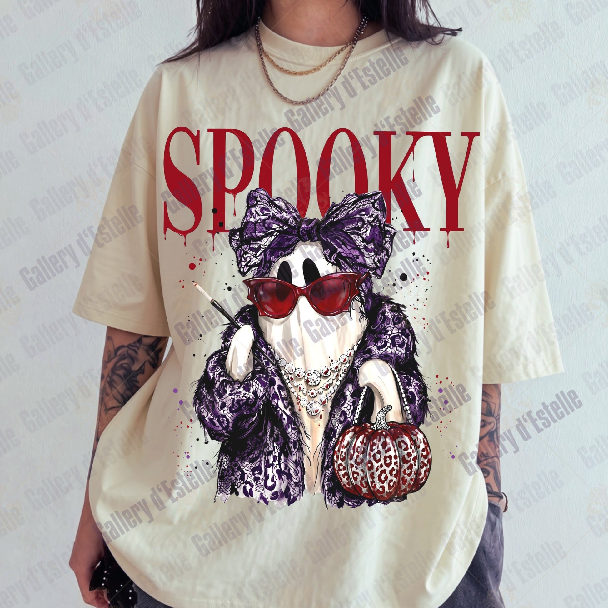 A person wearing an oversized cream-colored graphic t-shirt with a 'Spooky' glam ghost character print in purple leopard print, red sunglasses, and holding a pumpkin.