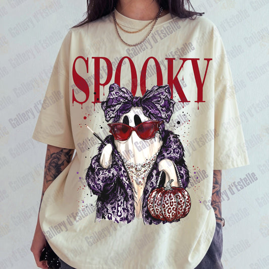 A person wearing an oversized cream-colored graphic t-shirt with a 'Spooky' glam ghost character print in purple leopard print, red sunglasses, and holding a pumpkin.