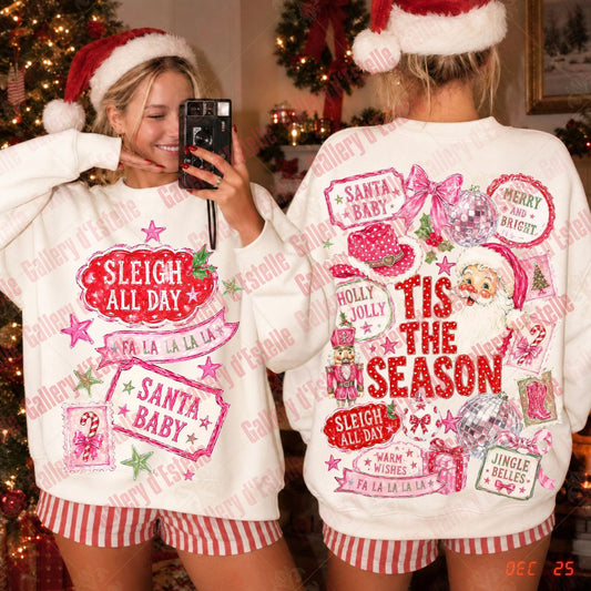 Two women wearing matching Christmas-themed white sweatshirts with red and pink holiday graphics, shown in a mirror selfie in front of a decorated Christmas tree. One view shows the front design and the other shows the back design with text including 'Sleigh All Day', 'Santa Baby', 'Tis the Season', and 'Merry and Bright'.