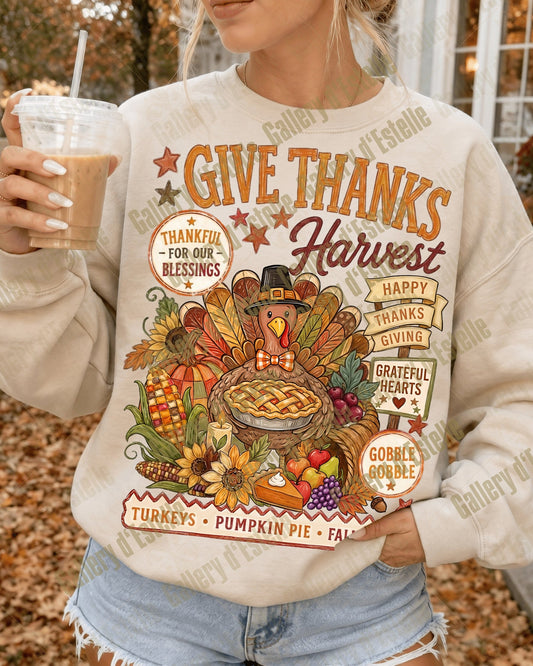 A woman wearing a cream-colored crewneck sweatshirt with a colorful autumn Thanksgiving graphic, holding an iced coffee in an outdoor fall setting.