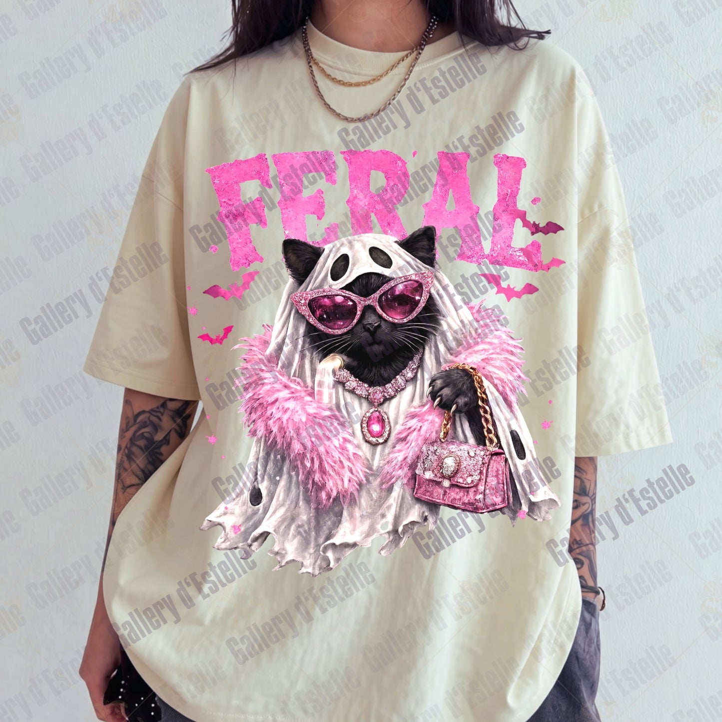 A person wearing an oversized cream-colored graphic t-shirt featuring a stylized black cat dressed in pink sunglasses, a white veil, and a pink fluffy boa under the word 'FERAL' in pink. 