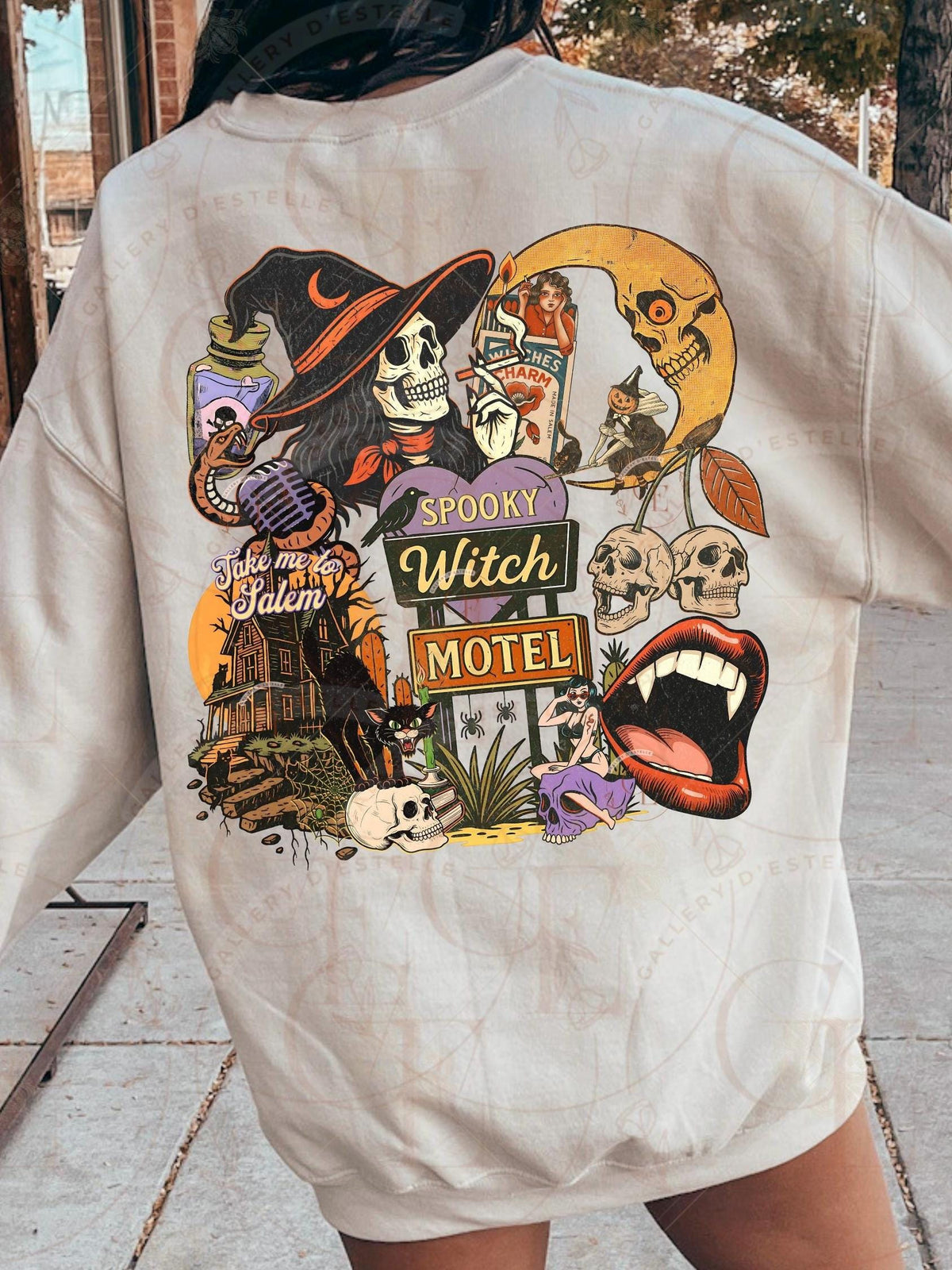 Beige t-shirt with Halloween-themed graphic design featuring skeletons, witches, and a motel sign.