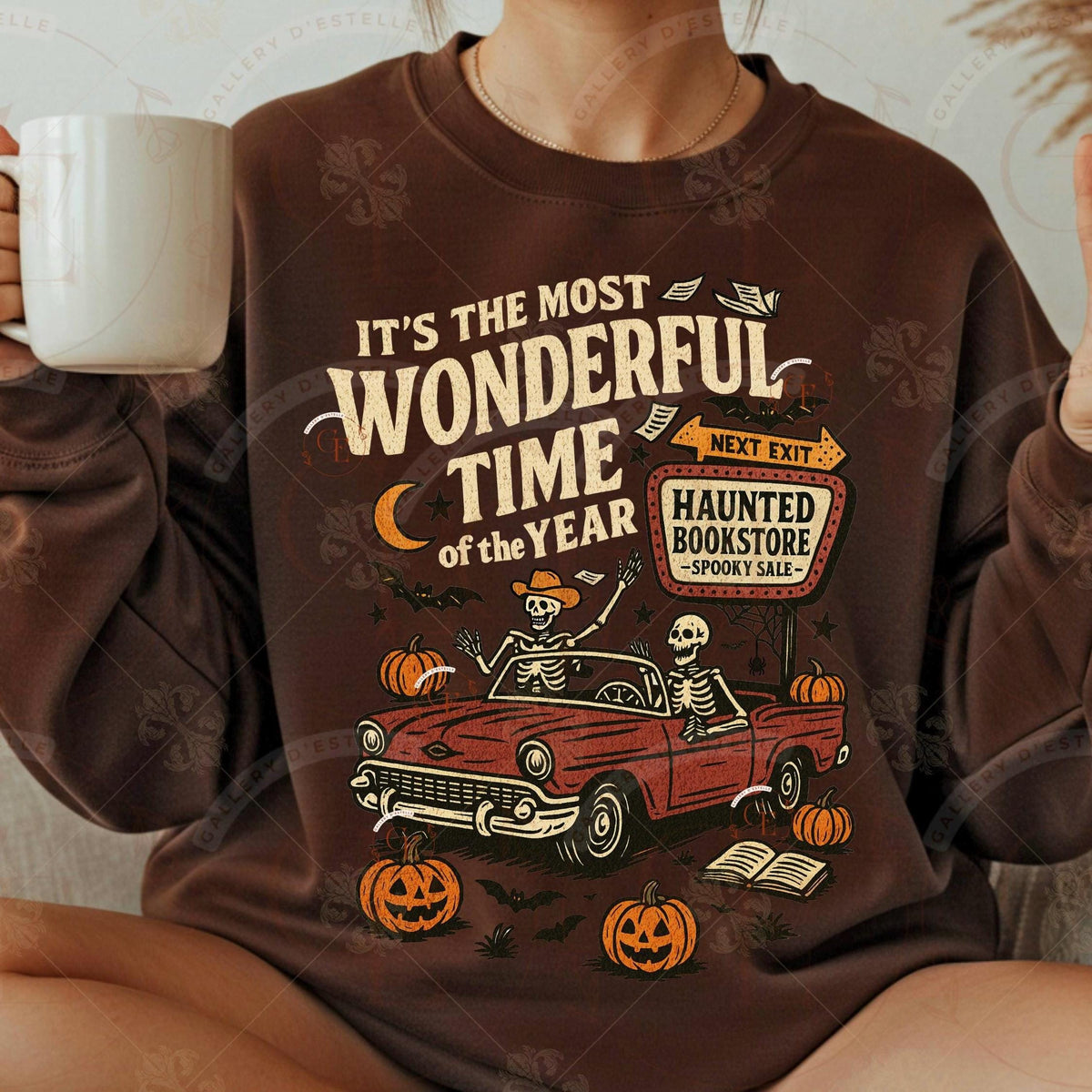 Person wearing a Halloween-themed sweatshirt with a graphic of a red car, skeletons, pumpkins, and text.