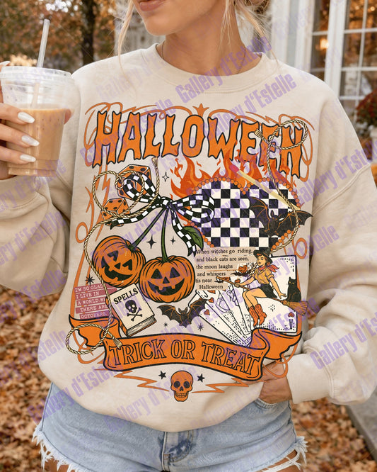 A woman wearing a cream-colored crewneck sweatshirt with a colorful Halloween graphic print featuring pumpkins, bats, ghosts, and the words 'HALLOWEEN' and 'TRICK OR TREAT'. She is holding an iced coffee in an outdoor autumn setting.