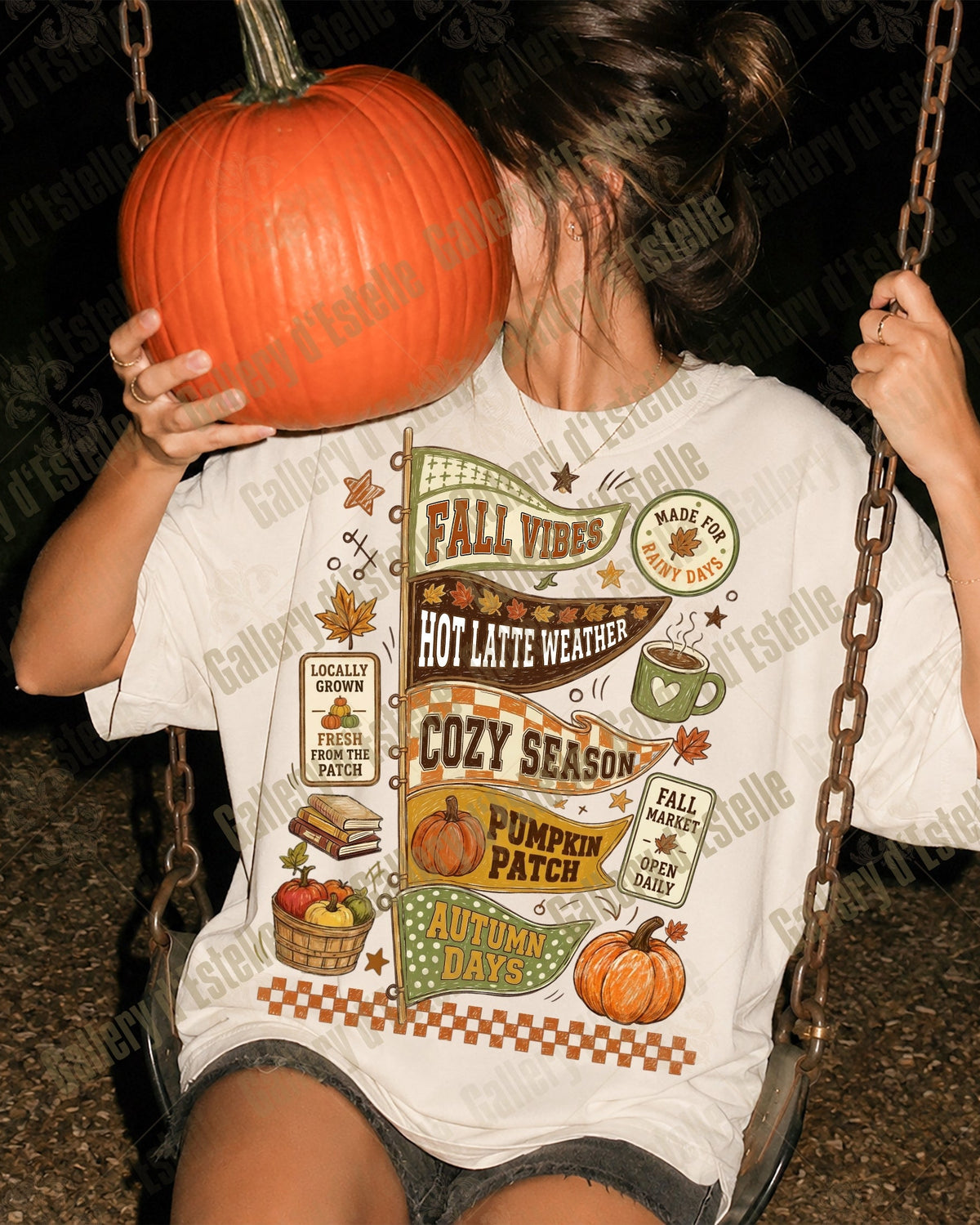 A person sitting on a swing at night wearing a white graphic t-shirt with autumn-themed illustrations and text, holding a large orange pumpkin in front of their face.