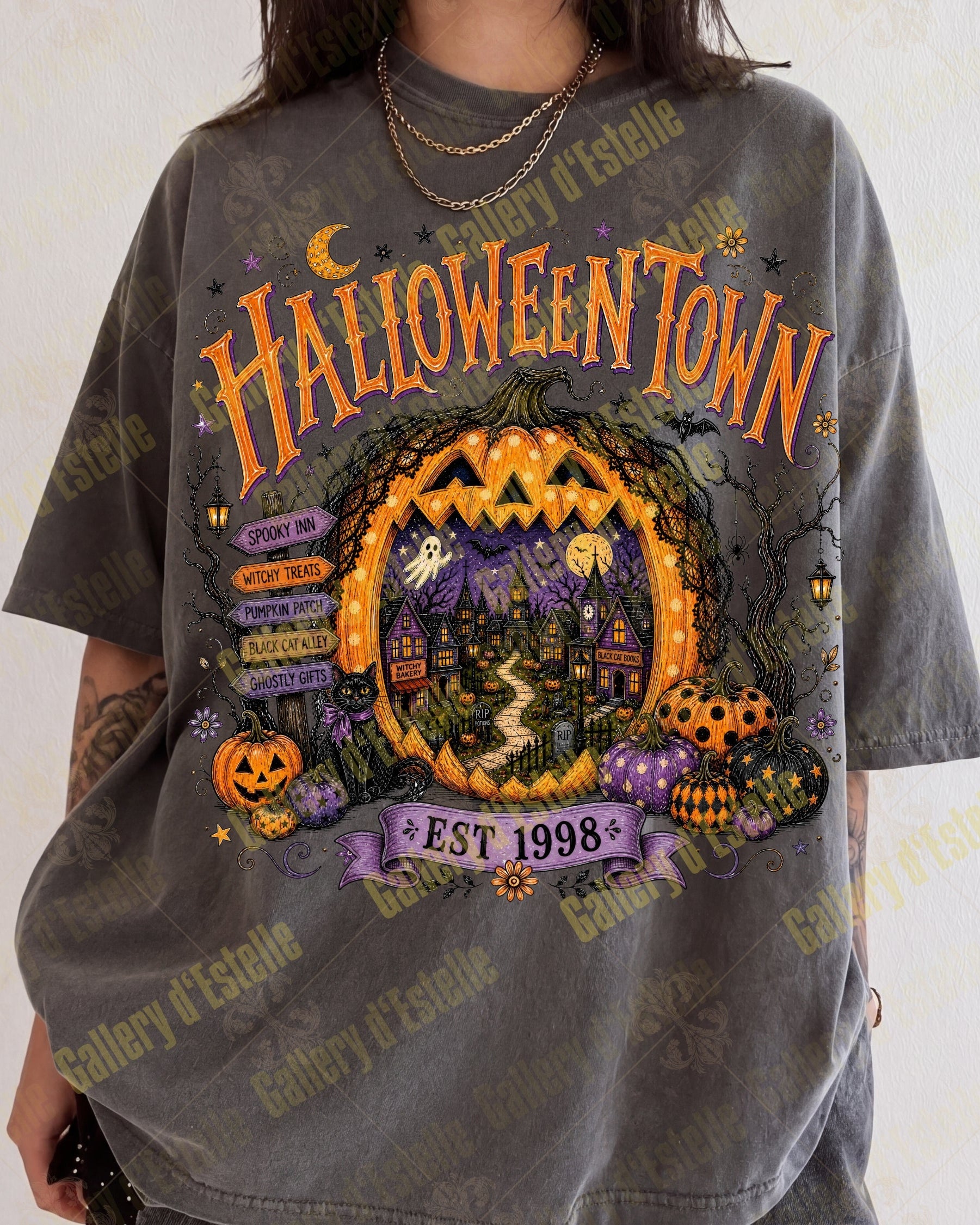 A person wearing an oversized dark gray graphic T-shirt with a colorful Halloween-themed print reading 'HALLOWEENTOWN' and 'EST 1998', shown against a light neutral background.