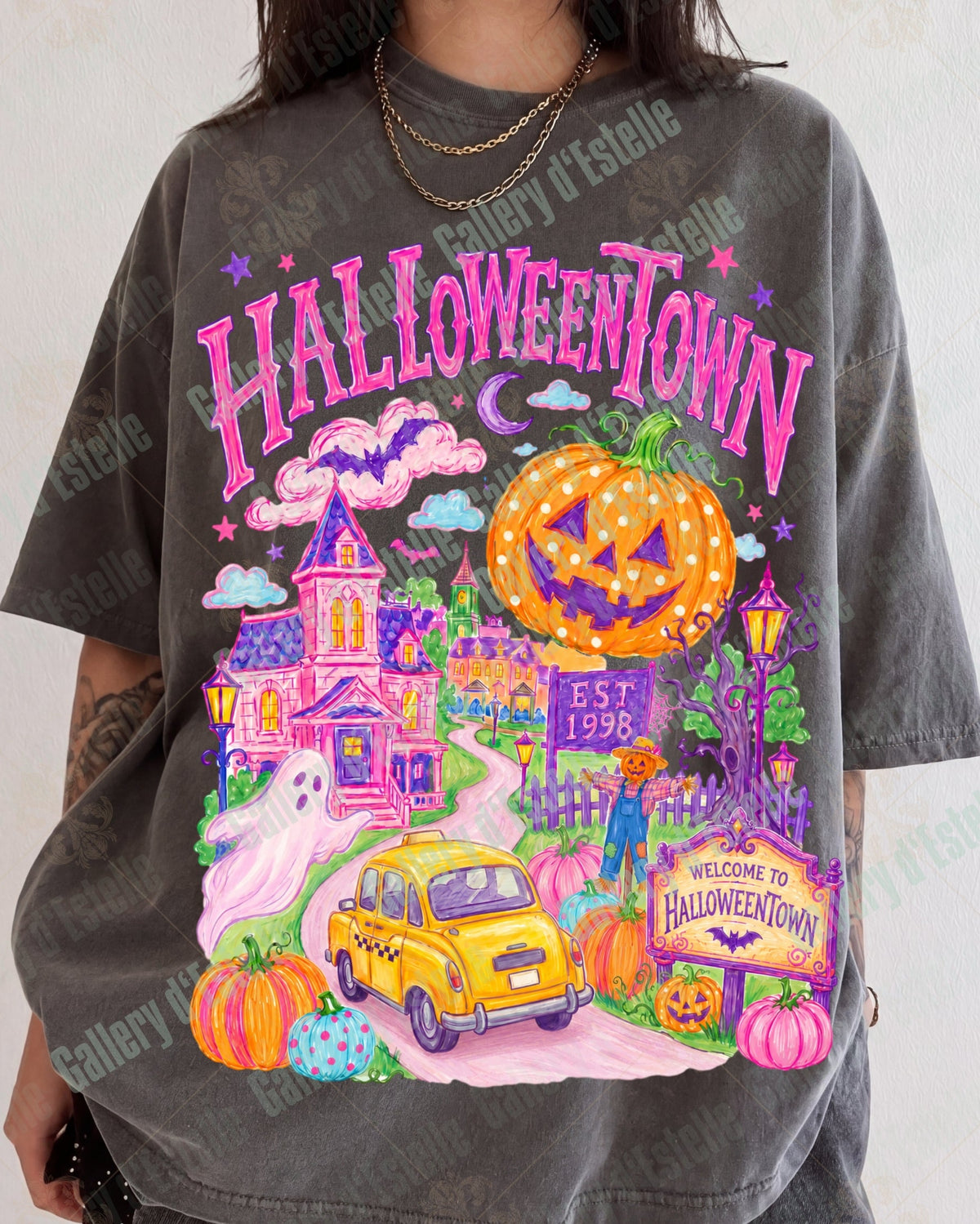 A person wearing an oversized dark gray graphic T-shirt with a colorful Halloween-themed print reading 'HALLOWEENTOWN' and featuring a jack-o'-lantern, haunted house, yellow car, and pumpkins.
