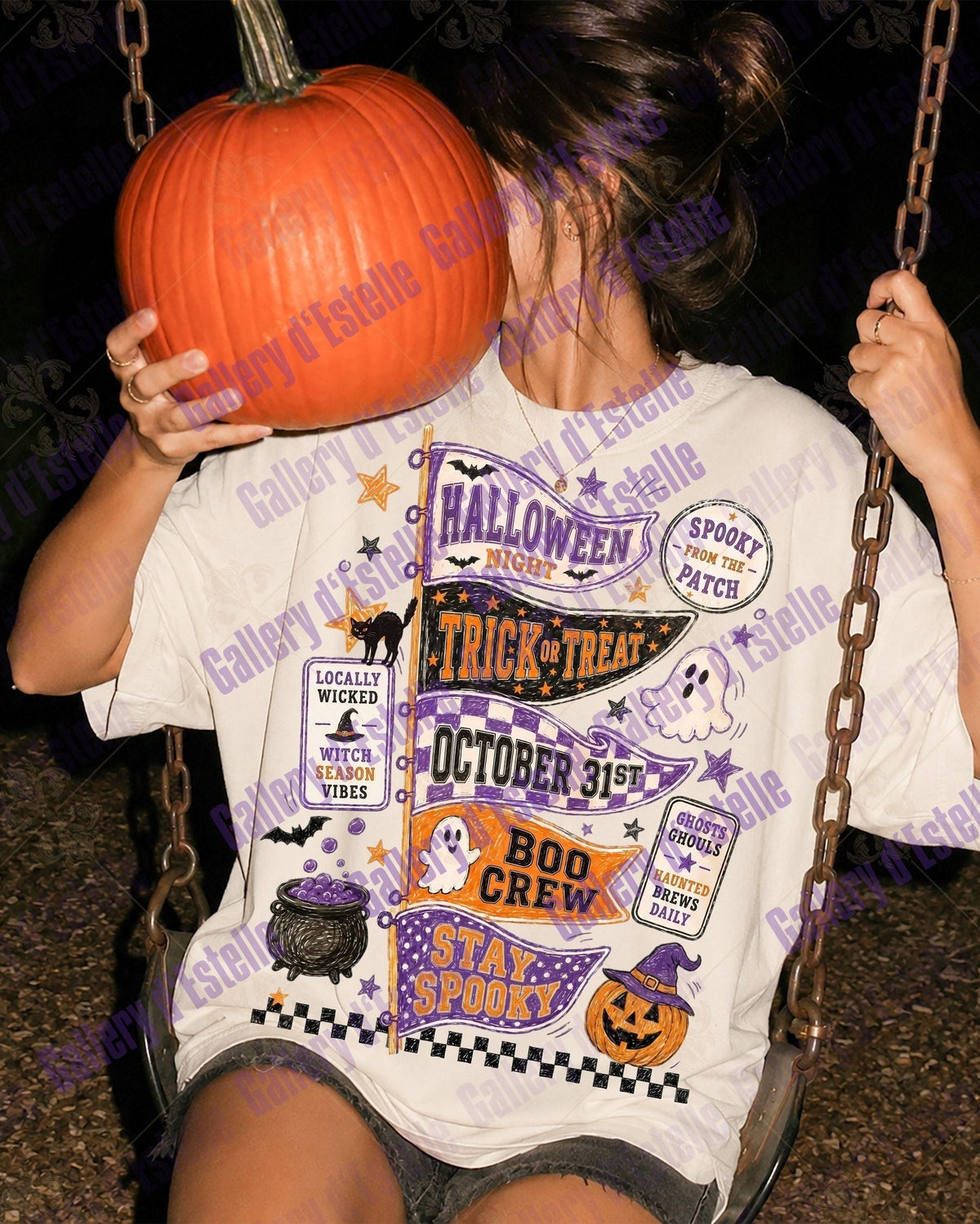 A person sitting on a swing at night wearing a white graphic T-shirt with Halloween-themed patch-style prints, while holding a large orange pumpkin in front of their face. The background is dark and outdoor.