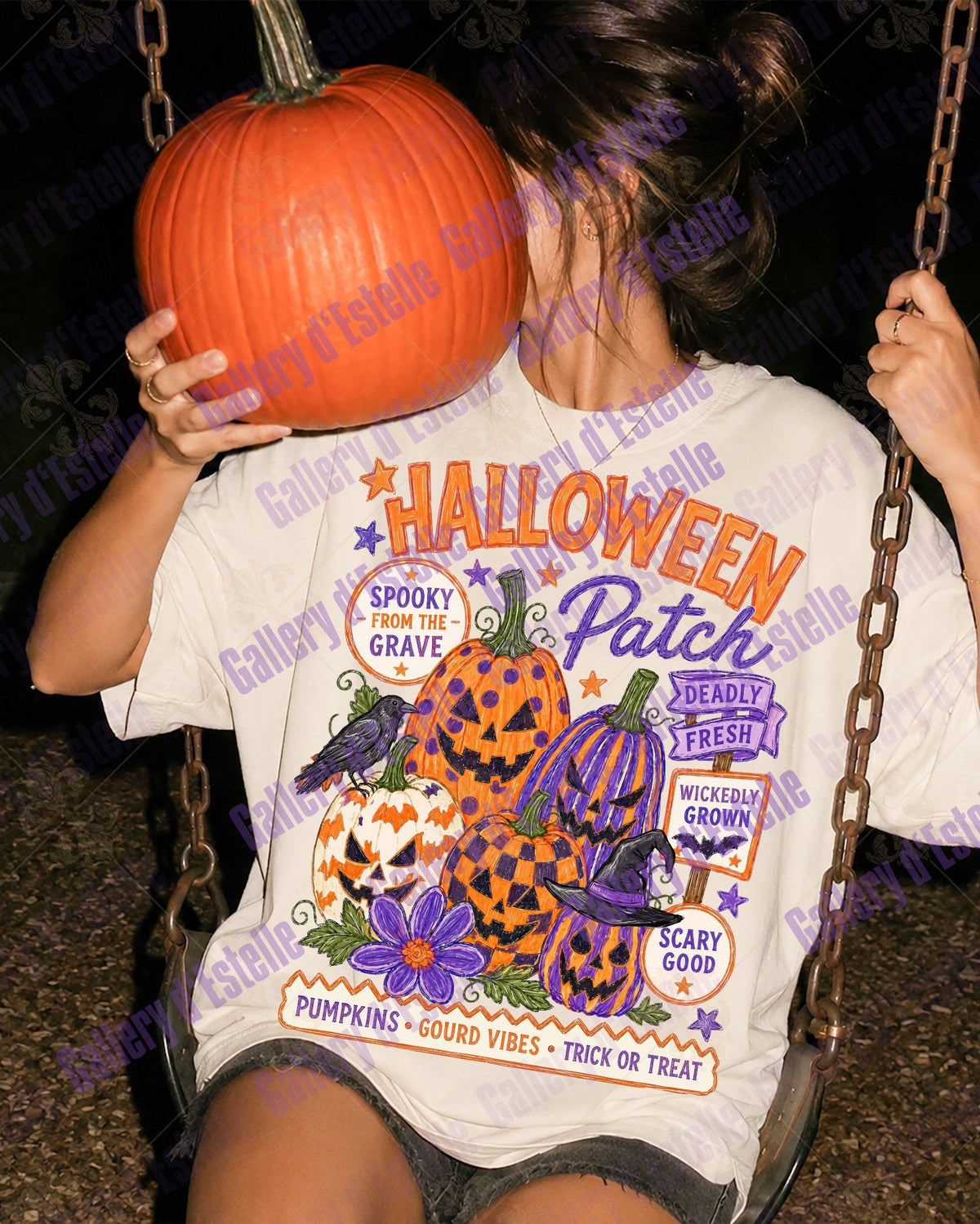 A person sitting on a swing at night wearing a white graphic T-shirt with a Halloween design. The shirt features orange and purple text reading 'Halloween Patch' with pumpkins, spiders, and purple flowers.