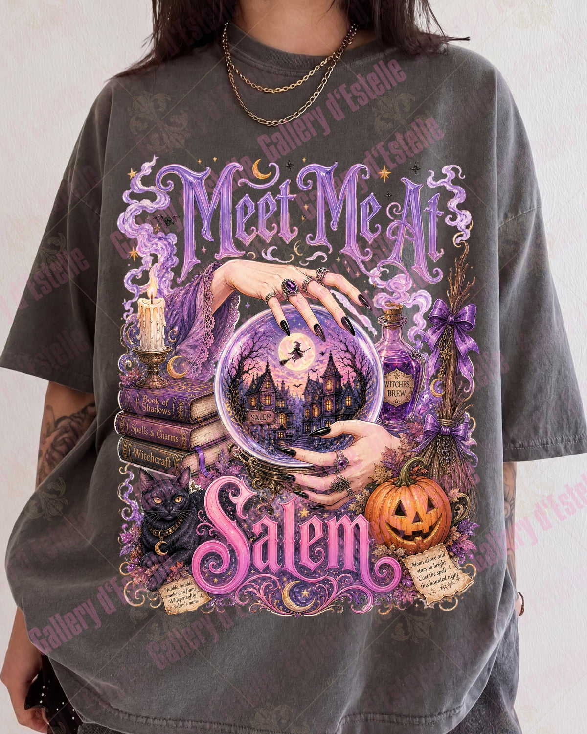 A person wearing an oversized dark gray graphic T-shirt with a large Halloween-themed print featuring purple gothic lettering that reads 'Meet Me At Salem,' a crystal ball, witch hands, candles, books, and a jack-o'-lantern.