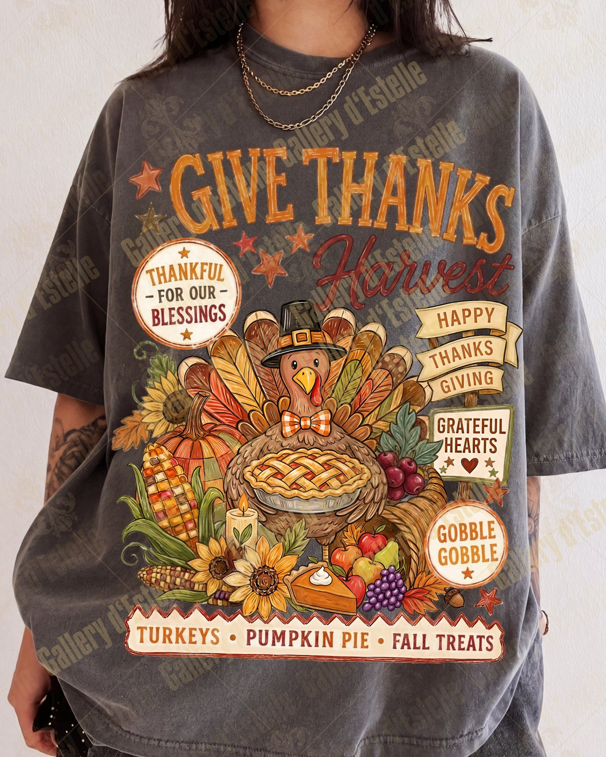 A person wearing an oversized dark gray graphic T-shirt with a colorful Thanksgiving harvest design featuring a turkey, pie, pumpkins, and autumn text.