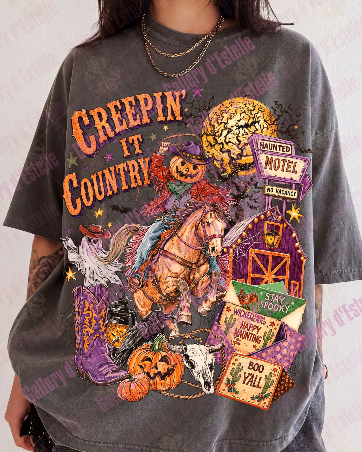 A person wearing an oversized dark gray graphic T-shirt with a colorful Halloween-themed print reading 'Creepin' It Country' and featuring pumpkins, a horse, a haunted motel, and spooky illustrations.