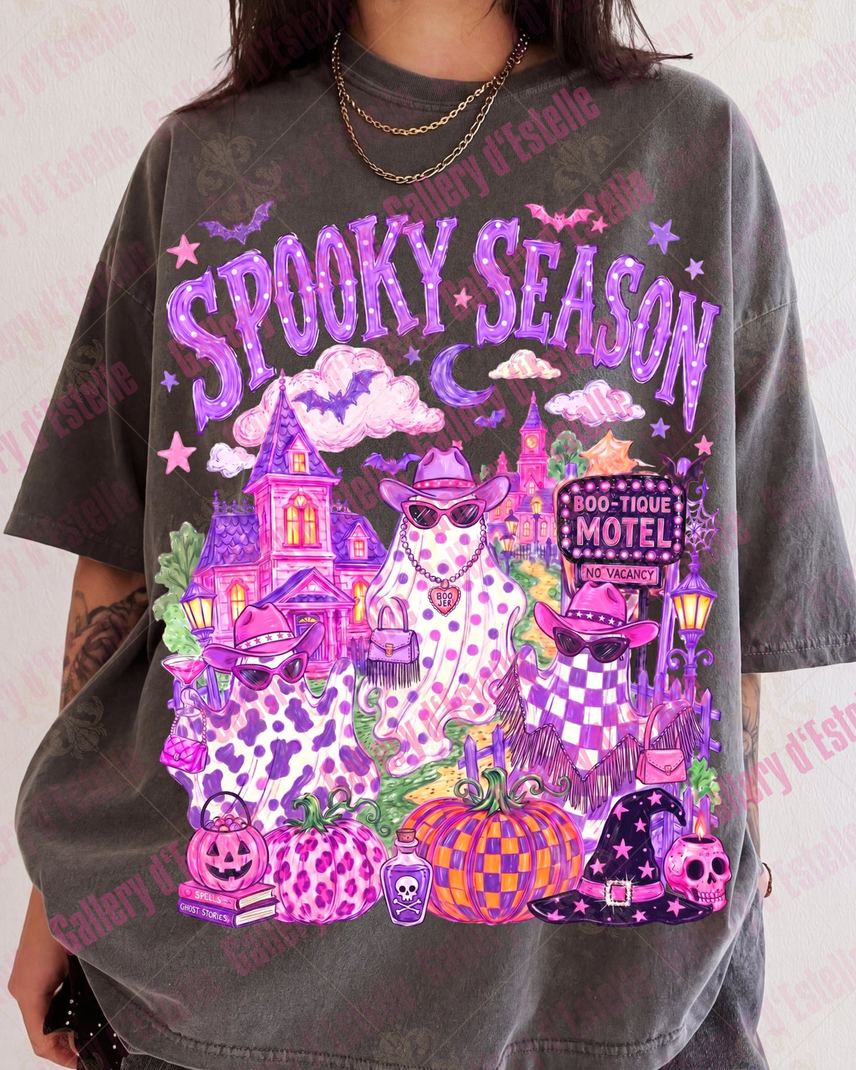 A person wearing a faded charcoal gray graphic t-shirt with a vibrant purple and pink 'Spooky Season' Halloween design featuring three cowgirl ghouls, a haunted house, pumpkins, and a witch hat.