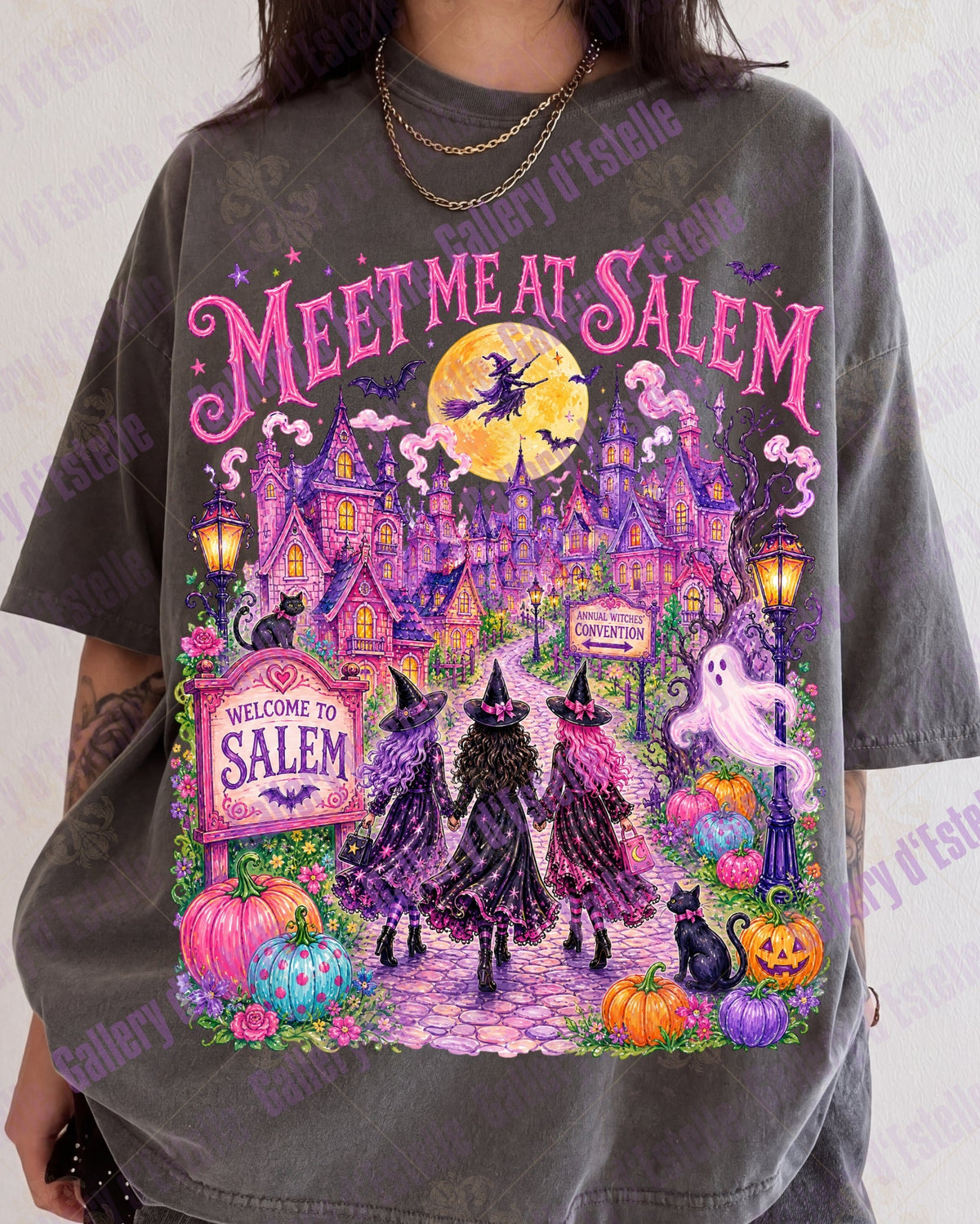 A person wearing an oversized faded charcoal gray graphic t-shirt with a colorful 'Meet Me at Salem' Halloween illustration featuring witches, a haunted house, pumpkins, and a ghost.