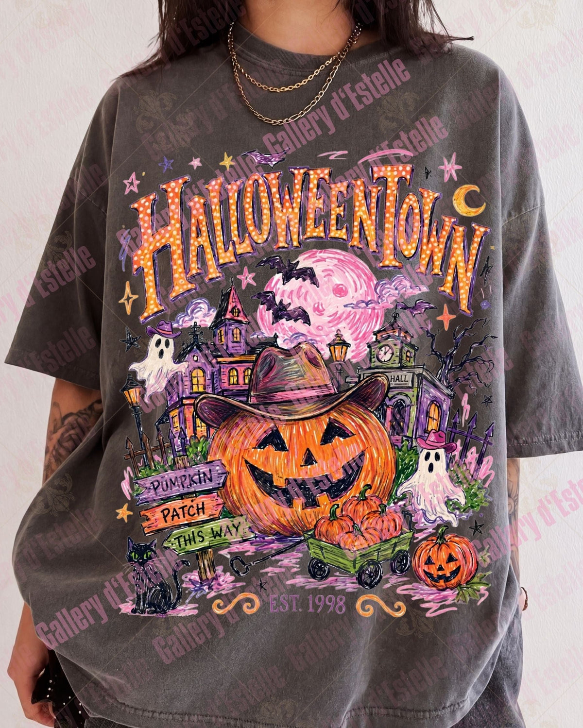 A person wearing an oversized dark gray graphic T-shirt with a colorful Halloween-themed print featuring pumpkins, ghosts, haunted houses, bats, and the text 'HALLOWEENTOWN'.