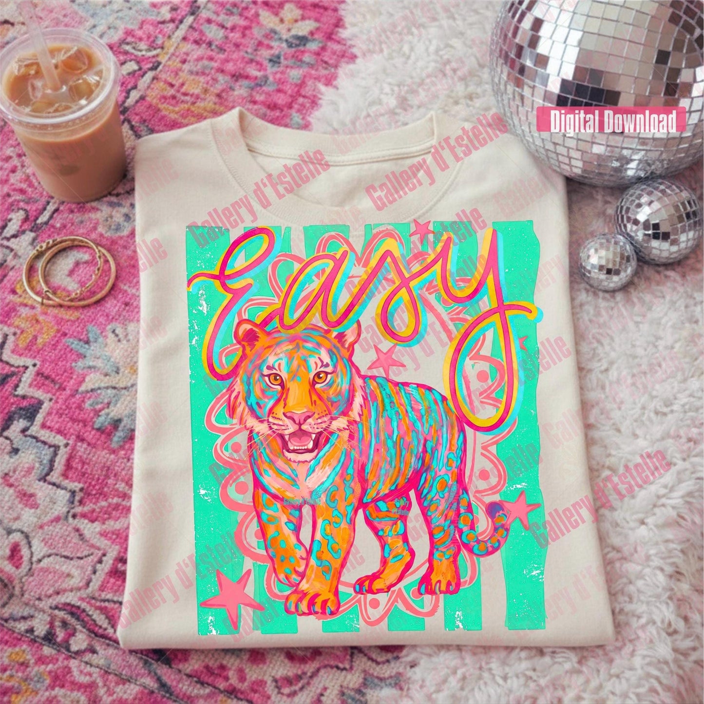T-shirt with a colorful tiger design and 'easy' text on a pink patterned surface with a drink and disco balls.