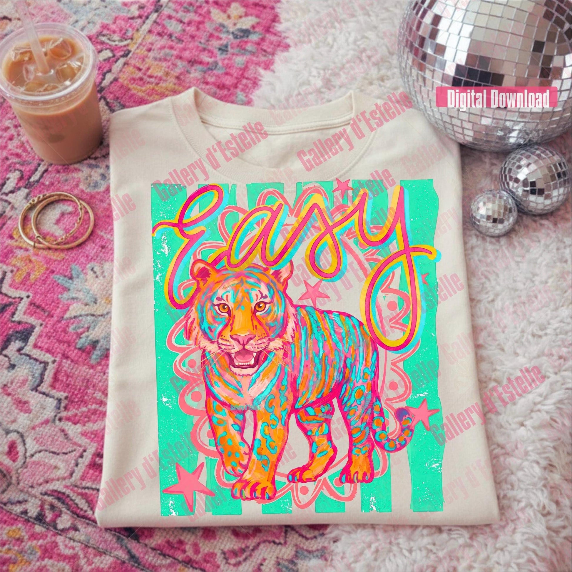 T-shirt with a colorful tiger design and 'easy' text on a pink patterned surface with a drink and disco balls.