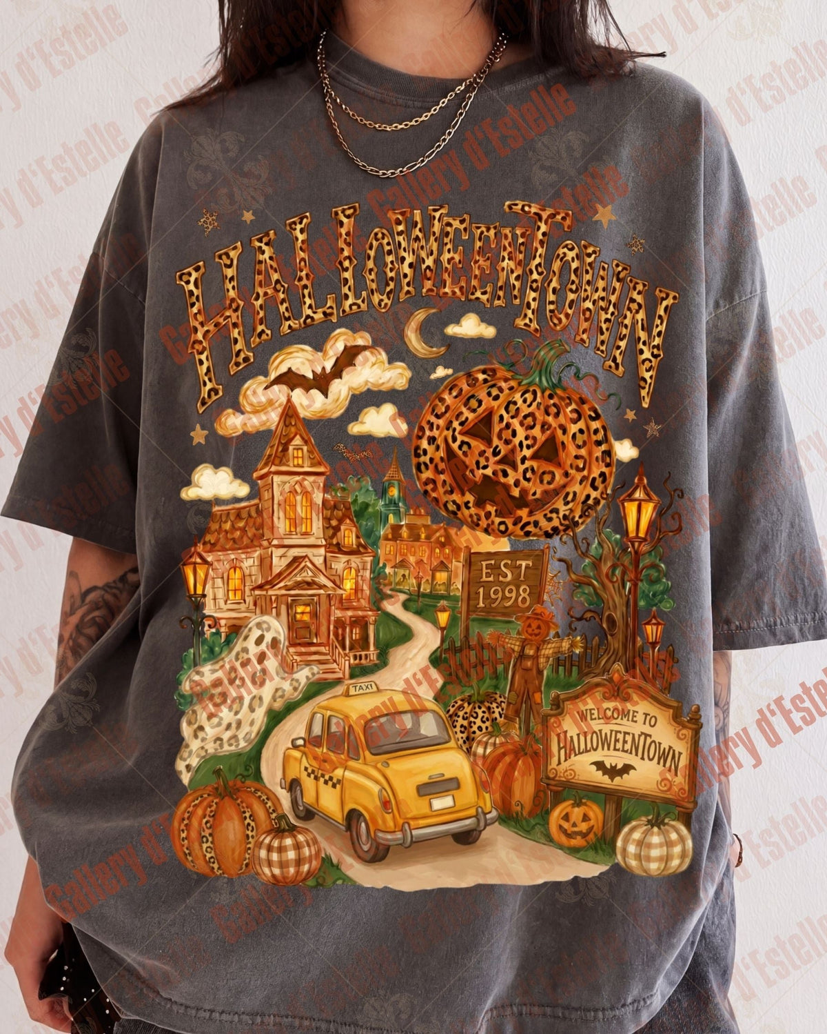 A person wearing an oversized dark gray graphic t-shirt with a detailed Halloween-themed print featuring pumpkins, a yellow car, a haunted house, and the word 'HALLOWEEN' in leopard print.