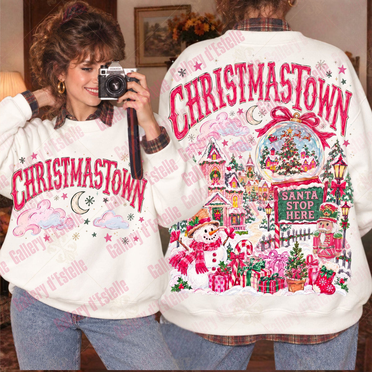A person modeling a white Christmas-themed sweatshirt, showing both the front and back views. The sweatshirt features 'CHRISTMASTOWN' in bold pink letters on the front, and a detailed Christmas village scene with snowman, Santa, gifts, and stars on the back.