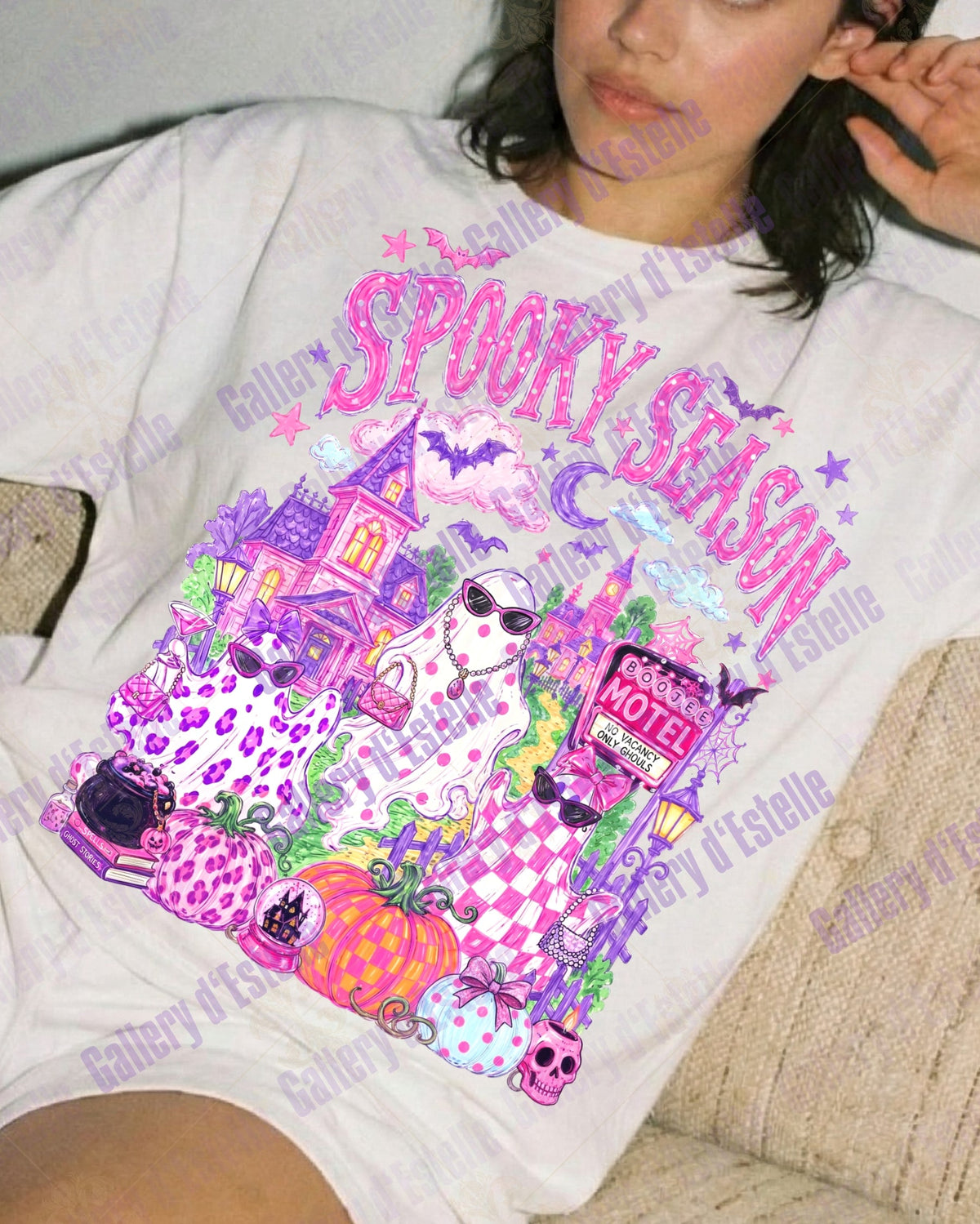 A woman reclining on a beige couch wearing a white graphic t-shirt with a colorful 'Spooky Season' Halloween print and matching white shorts.