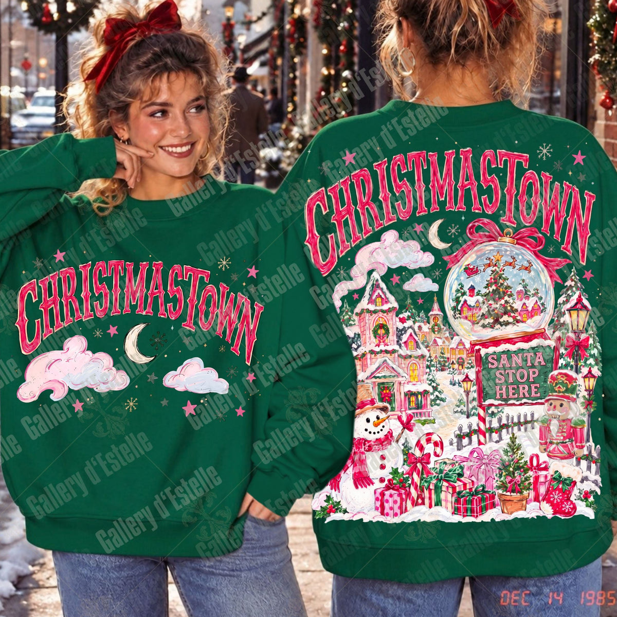 A green Christmas-themed sweatshirt shown on two models, displaying both the front and back designs. The front features the text 'CHRISTAMASTOWN' in pink with white clouds and a crescent moon.