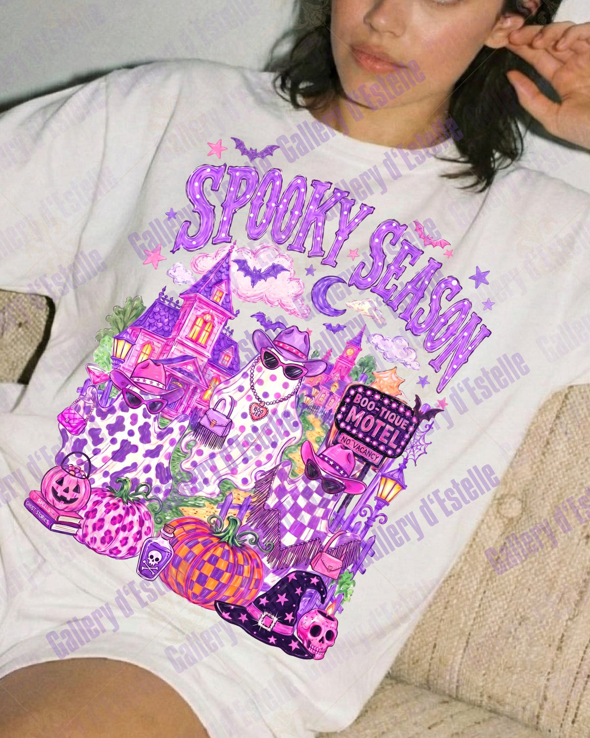 A woman reclining on a beige couch wearing a white graphic t-shirt with a colorful 'Spooky Season' Halloween design in purple, pink, and orange, paired with white shorts.