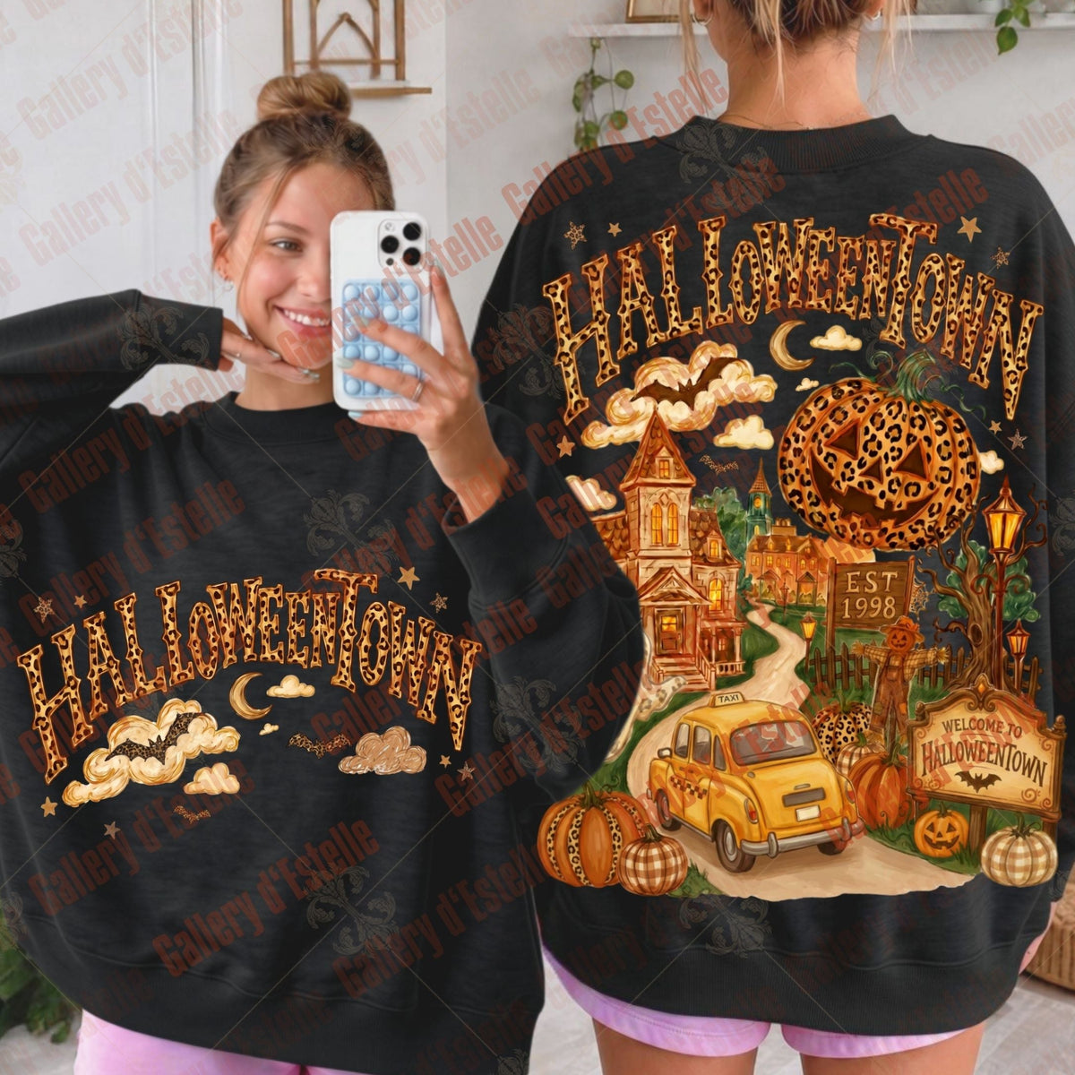 Two views of a black Halloween-themed sweatshirt featuring 'HALLOWEETOWN' text and a spooky town illustration with pumpkins, a yellow car and a haunted house. One view shows the front with a mirror selfie of a woman, and the other shows the back of the sweatshirt.