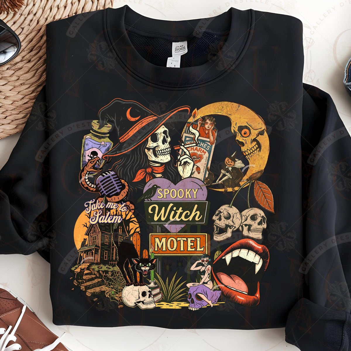 Black sweatshirt with Halloween-themed design featuring skulls, a witch skeleton, and a motel sign.