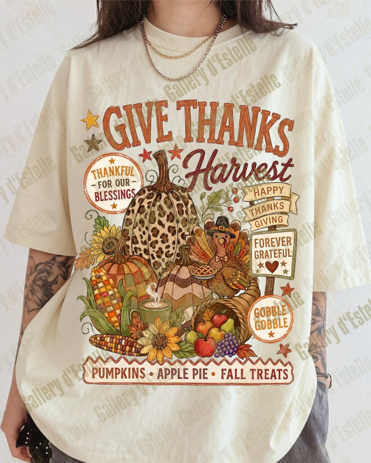 A person wearing an oversized cream-colored graphic T-shirt with a fall harvest design featuring pumpkins, turkeys, autumn leaves, and text including 'GIVE THANKS Harvest' and 'PUMPKINS • APPLE PIE • FALL TREATS'.