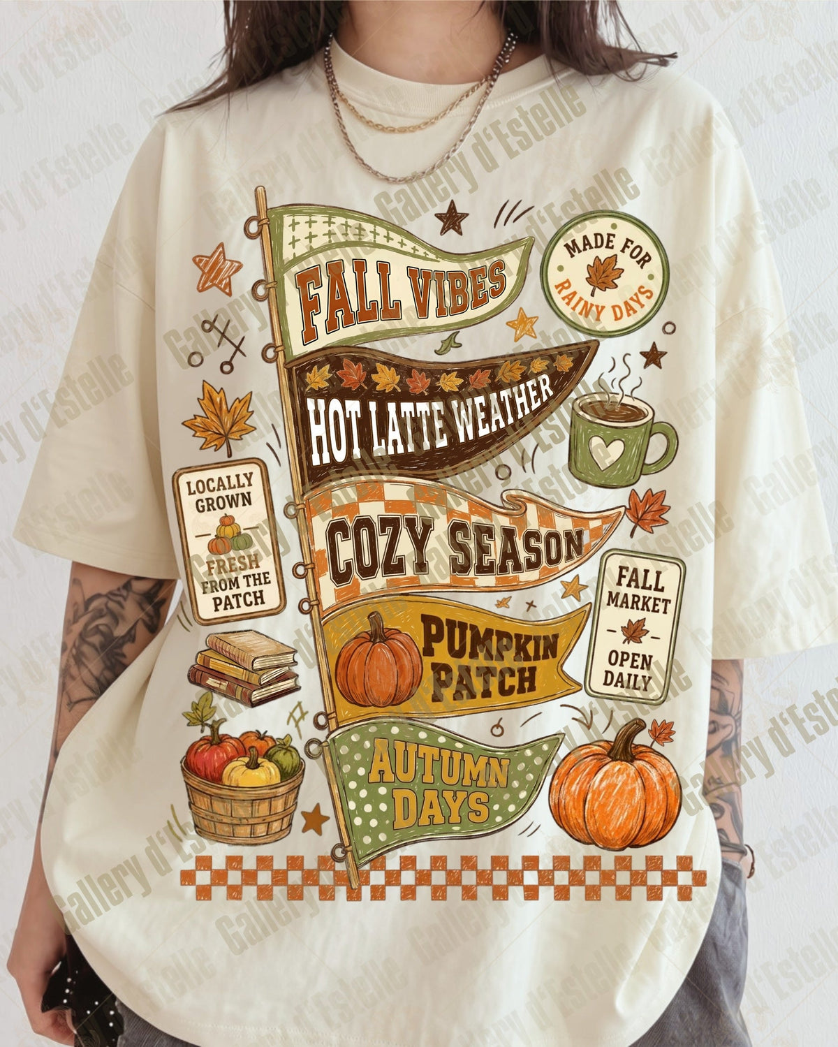 A person wearing a cream-colored graphic t-shirt with a colorful autumn-themed print featuring pumpkins, fall leaves, a coffee cup, and seasonal text like 'FALL VIBES' and 'COZY SEASON'.