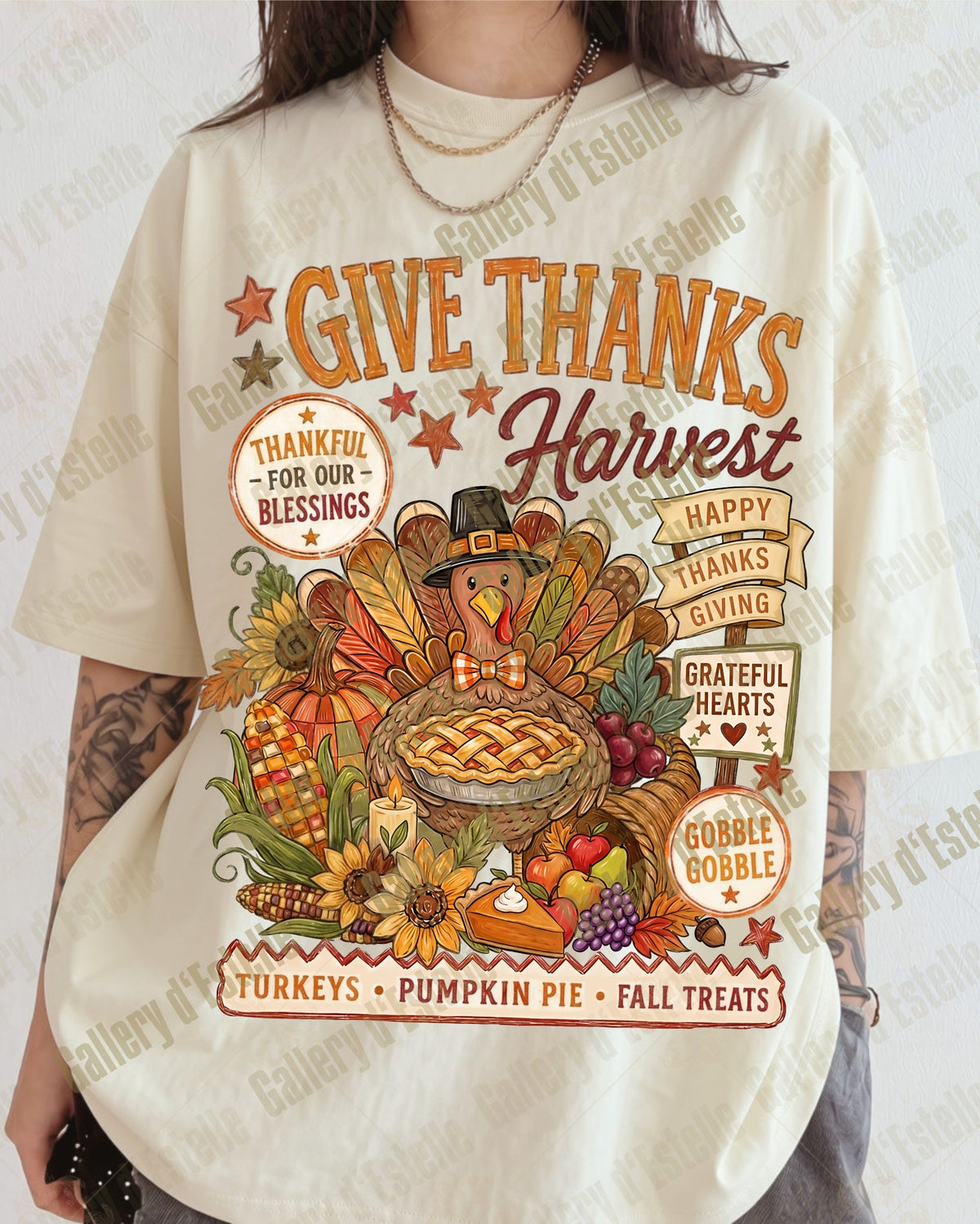 A person wearing an oversized cream-colored graphic T-shirt with a colorful autumn harvest design featuring a turkey, pumpkin pie, pumpkins, and the text 'GIVE THANKS Harvest'.