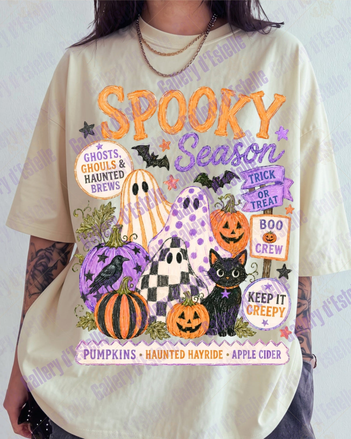 A person wearing an oversized cream-colored graphic t-shirt with a colorful 'Spooky Season' Halloween print featuring pumpkins, ghosts, a black cat, and bats.