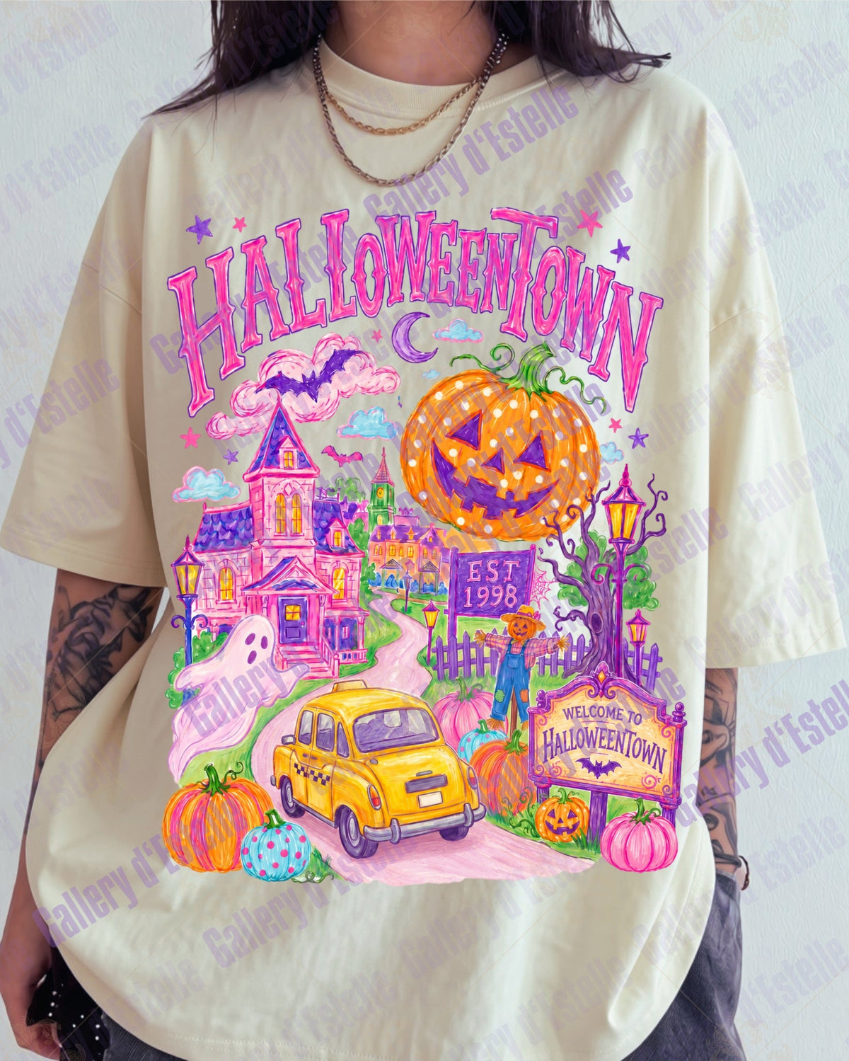 A person wearing an oversized cream-colored graphic t-shirt with a colorful Halloween-themed print featuring a jack-o'-lantern, haunted house, yellow car, and 'HALLOWEENTOWN' text.