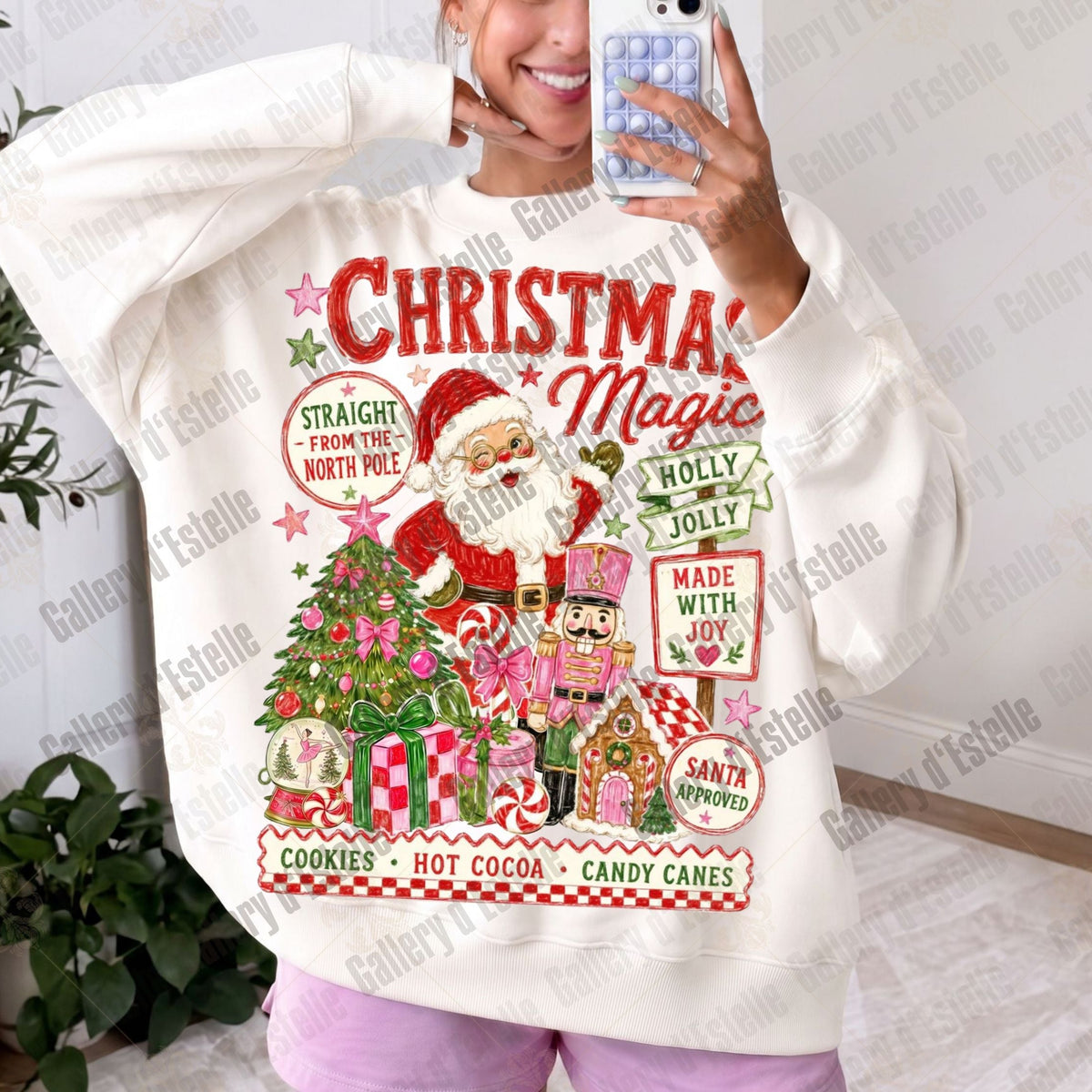 A woman takes a mirror selfie wearing an oversized cream-colored sweatshirt with a colorful Christmas graphic print featuring Santa Claus, a Christmas tree, and festive text.