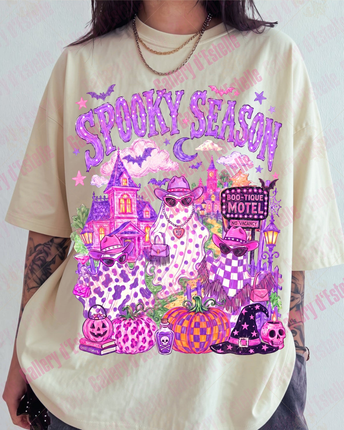 A person wearing an oversized cream-colored graphic t-shirt with a vibrant purple and pink 'Spooky Season' Halloween design featuring a haunted house, cowgirl ghosts and pumpkins.